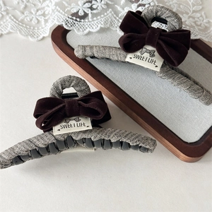 Detail view of large grey woven hair claw with a vintage brown velvet bow and label