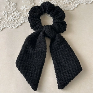 Detail of handmade crocheted black hair scrunchie with long bow and knitted texture