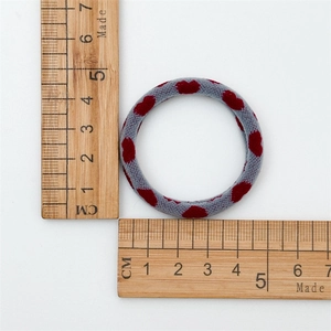 Macro shot of a gray elastic hair tie with red heart patterns next to a measuring ruler