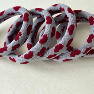 Close-up of four elastic towel hair ties with red heart patterns on grey knit fabric
