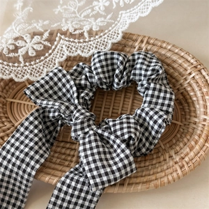 Classic black and white gingham checkered hair scrunchie with long bow ribbon on rattan tray