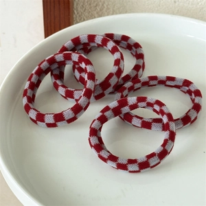 Close-up of five red and white checkerboard knit elastic hair ties on a ceramic plate