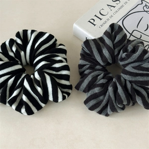Close-up of knit striped scrunchies in black, white, and grey on a textured stone surface