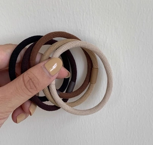 Dettaglio di elastici per capelli a costine resistenti in toni della terra in mano