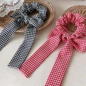 Close-up of red and black plaid scrunchies with long ribbons on a rustic woven tray