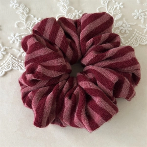 Close-up of a striped knit scrunchie in burgundy and pink with soft lace details