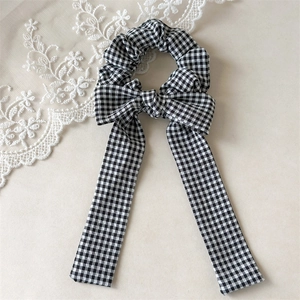 Close-up of black and white gingham hair scrunchie with long ribbon bow on lace background