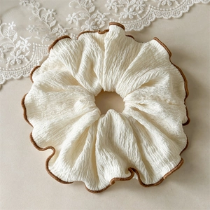 Détail d'un grand chouchou crème avec bord surjeté marron et tissu en crêpe texturé