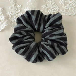 Detail view of black and grey striped knitted scrunchie on beige background with lace