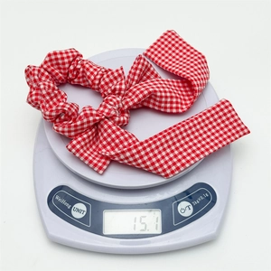 Macro detail of a red gingham bow scrunchie showing its weight of 15.1g on a digital scale