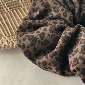 Detailed macro view of retro double-layer leopard velvet scrunchie on woven tray