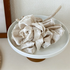 Vue détaillée d'un chouchou en velours beige avec pétales de fleurs plissés sur socle