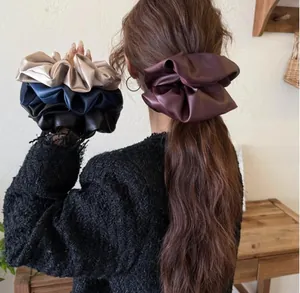 Detail view of thick satin scrunchies in various colors worn on a ponytail style