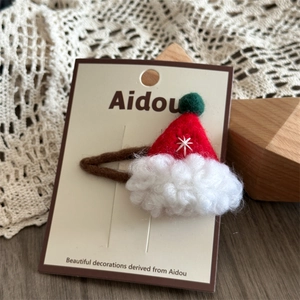 Close-up of a red felt Santa hat hair clip with white snowflake embroidery and green pompom