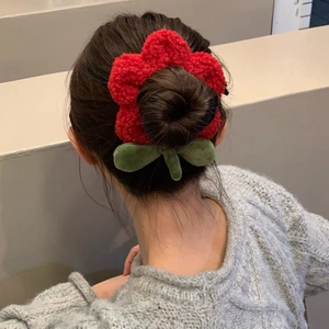 Detalle de coletero de flor de felpa roja con hojas verdes sobre un peinado de moño