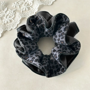 Close-up detail of leopard print velvet scrunchie with black leather trim and stitching