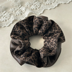 Detailed view of the leopard print and brown leather stitching on the velvet scrunchie