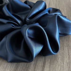 Macro shot of the navy blue satin scrunchie showing detailed silk texture and soft sheen
