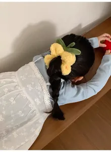 Detalle de un coletero de felpa amarillo con forma de flor usado por una niña en casa