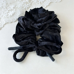 Détail macro du chouchou en velours noir avec rose 3D et rubans en nœud