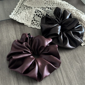Detail of oversized satin scrunchies in dark brown and wine red with rich silk-like texture