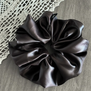 Close-up of thick dark brown satin hair scrunchie with subtle logo label on lace