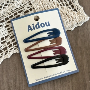 Detail of four colorful metal drop hair clips on cardstock over a lace table runner