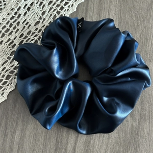 Detail of navy blue oversized satin scrunchie with silky sheen and soft folds