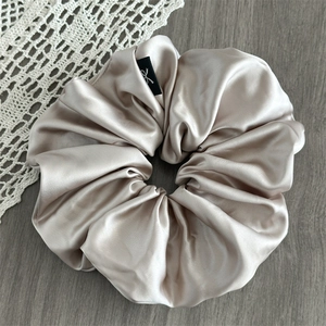 Detail view of champagne satin oversized scrunchie with elegant logo label and silk texture