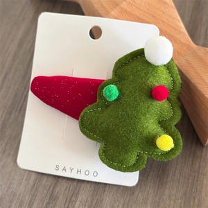 Detail of green felt Christmas tree hair clip with colorful pom-poms on a festive red base