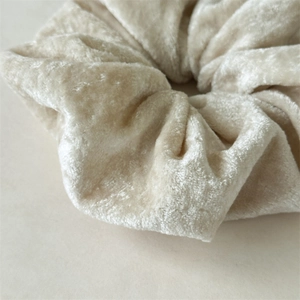 Makroaufnahme von cremefarbenem Samt-Haargummi mit weicher Textur und plissierten Details