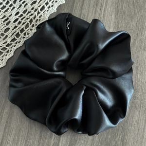 Macro detail of high-shine black satin oversized scrunchie with elegant logo tag on wood