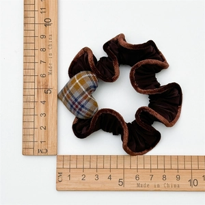 Détail d'un chouchou en velours marron avec pendentif cœur à carreaux et règle de mesure