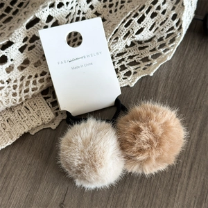Dettaglio di elastici per capelli in morbida ecopelliccia beige e marrone su legno