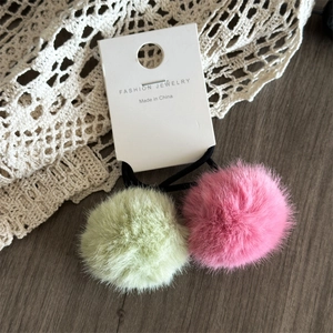 Dettaglio degli elastici per capelli con pompon rosa e verdi su sfondo di pizzo decorativo