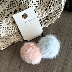 Dettaglio degli elastici per capelli con pompon in peluche rosa e blu su pizzo beige