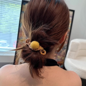 Detailed view of an elastic coil hair tie with a soft yellow felt ball on braided band