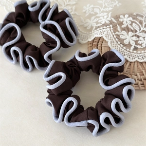 Close-up of two pleated dark brown fabric scrunchies with elegant light blue piping detail