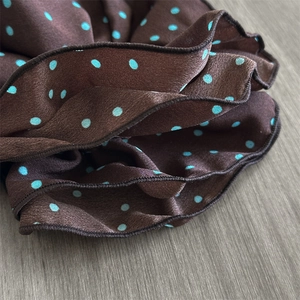 Detail of premium satin scrunchie featuring blue polka dots and delicate stitched edges