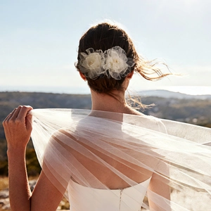 Détail de deux barrettes fleurs en tulle blanc sur un chignon de mariée élégant avec voile