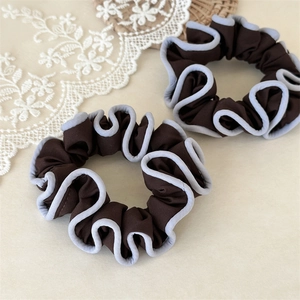 Detail of two brown fabric scrunchies with contrast piping and soft pleated texture