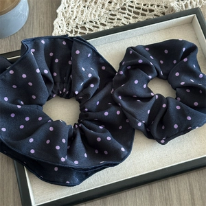 Set of two black satin scrunchies with purple polka dots displayed on a linen tray