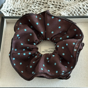 Detail of premium brown satin scrunchie with blue polka dots on a beige linen tray