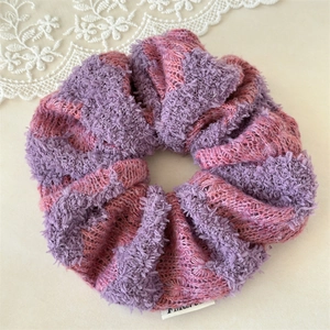 Close-up of a plush knitted scrunchie in purple and pink yarn with soft woven texture