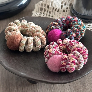 Close-up of knitted spiral hair ties with plush pom-poms on a rustic lace background