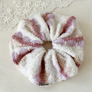 Detail of a knit scrunchie with beige and purple gradient colors and a brand tag