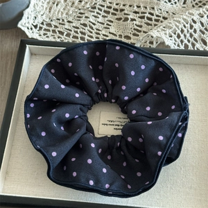 Close-up of large black satin scrunchie with purple polka dots on a display tray