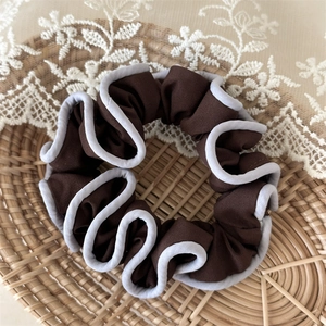 Detailed texture of ruffled fabric hair scrunchie in coffee brown with gray piping edge
