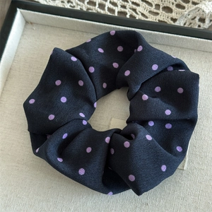 Detailed close-up of large satin black scrunchie with lavender dots on beige tray
