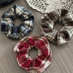 Close-up of three plaid scrunchies in navy, coffee, and burgundy on vintage lace